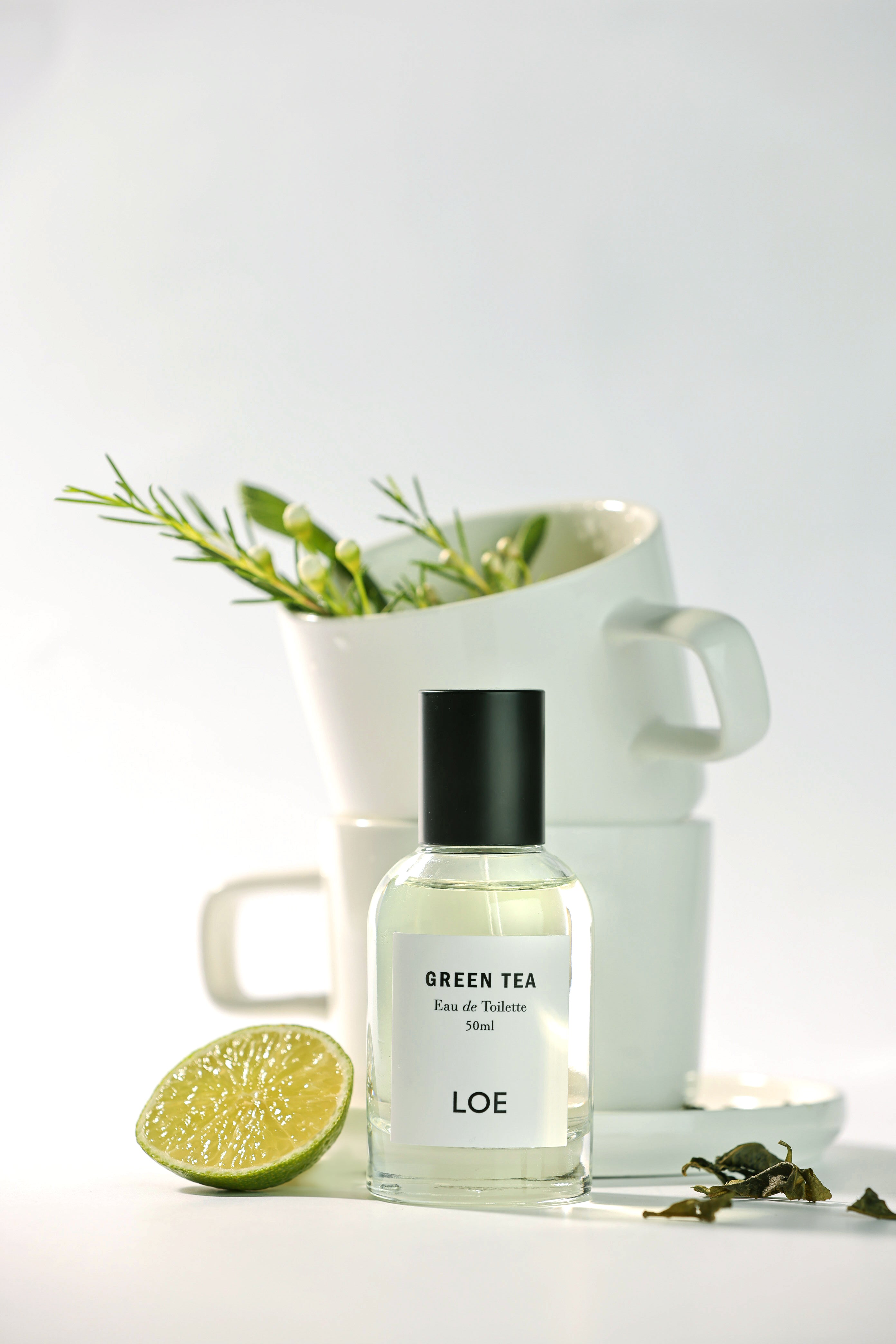 Perfume bottle labeled 'Green Tea' by LOE with a white pitcher and lime on a light background